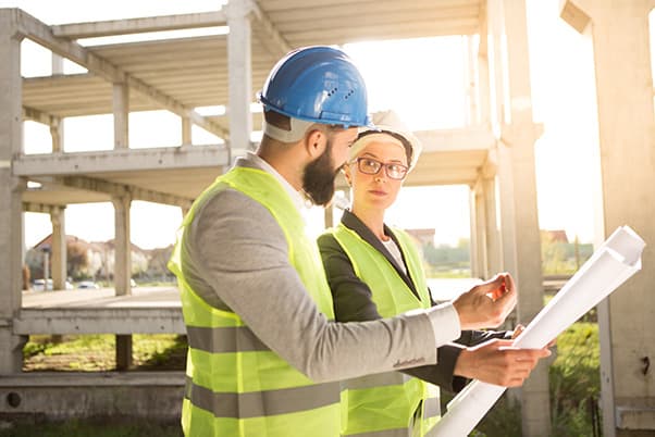 man and woman wearing hard hats and bright yellow vests in building under construction